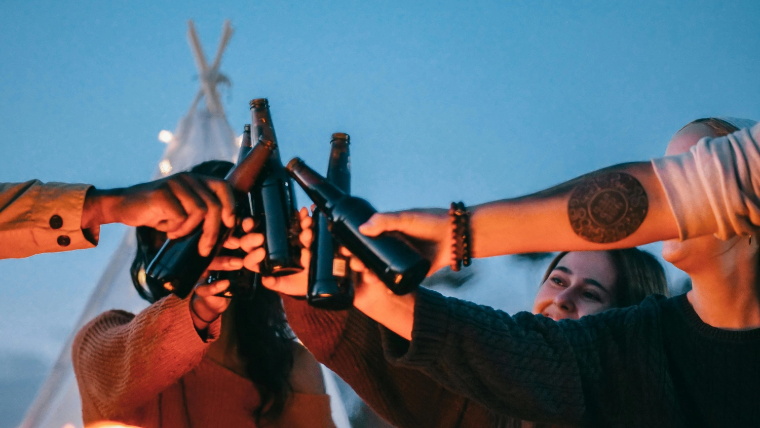 Hygge - Ferienwohnung - Dieses Bild fängt ein fröhliches Treffen von Freunden ein, die gemeinsam Bierflaschen anstoßen.